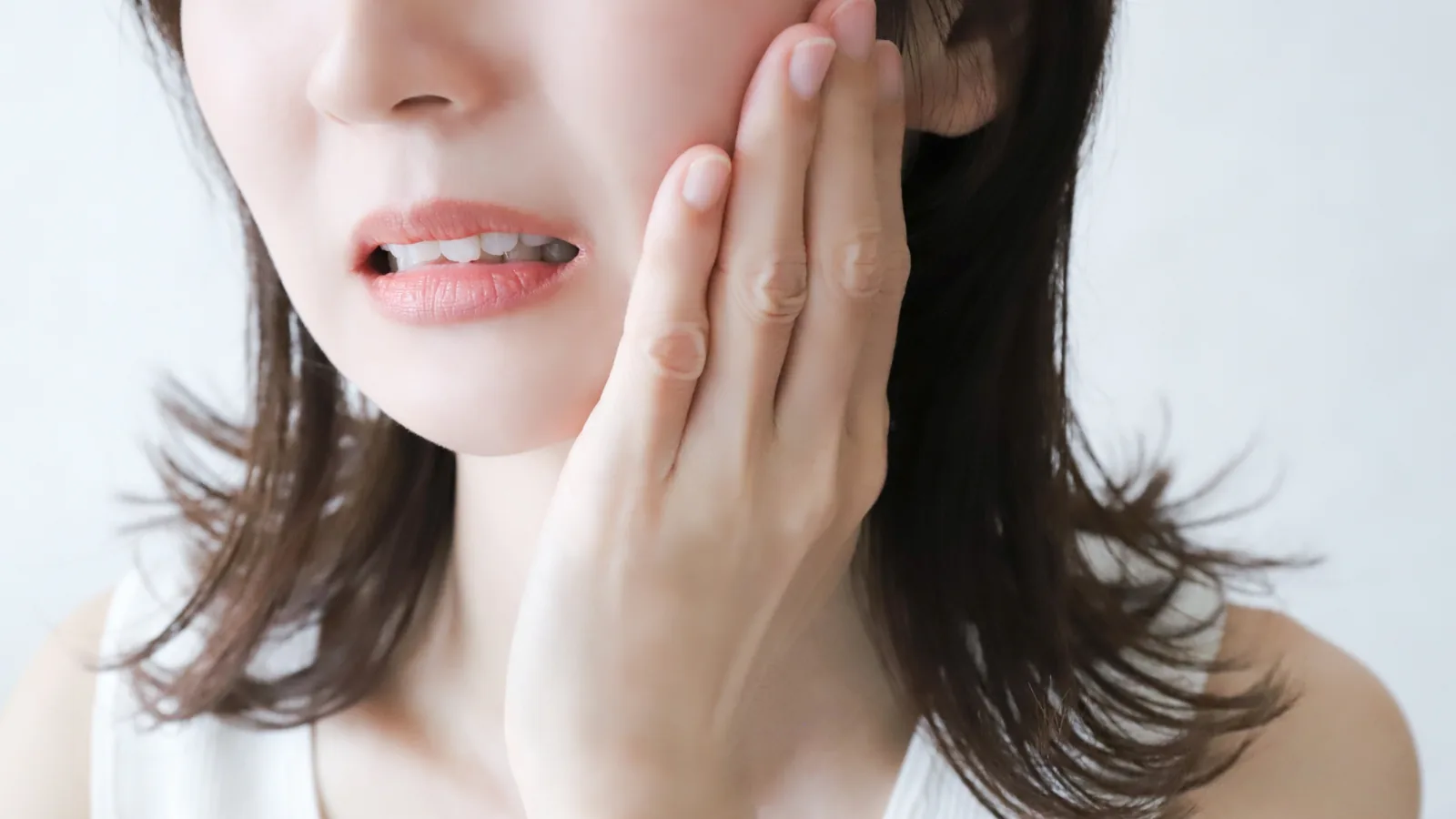 女性が頬を押さえて歯の痛みに顔をしかめている